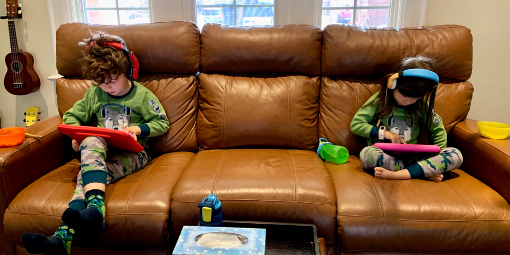 Two kids on couch with iPads and headphones