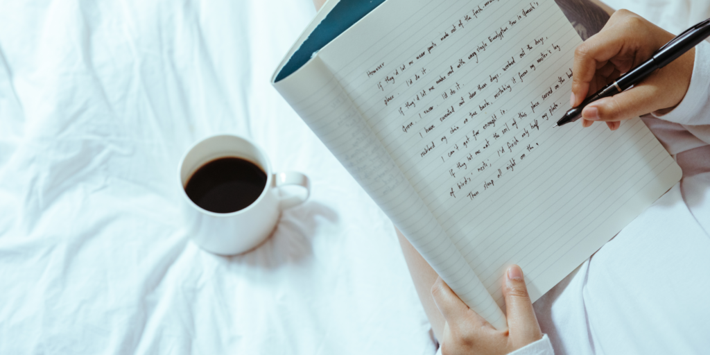 person writing in a journal with a cup of coffee on the bed